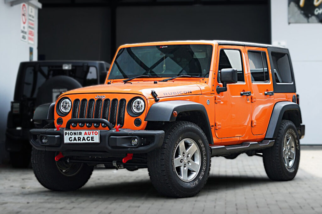 Tampilan depan Jeep JK oranye dengan bumper besi dan aksesoris modifikasi dari Pionir Auto Garage